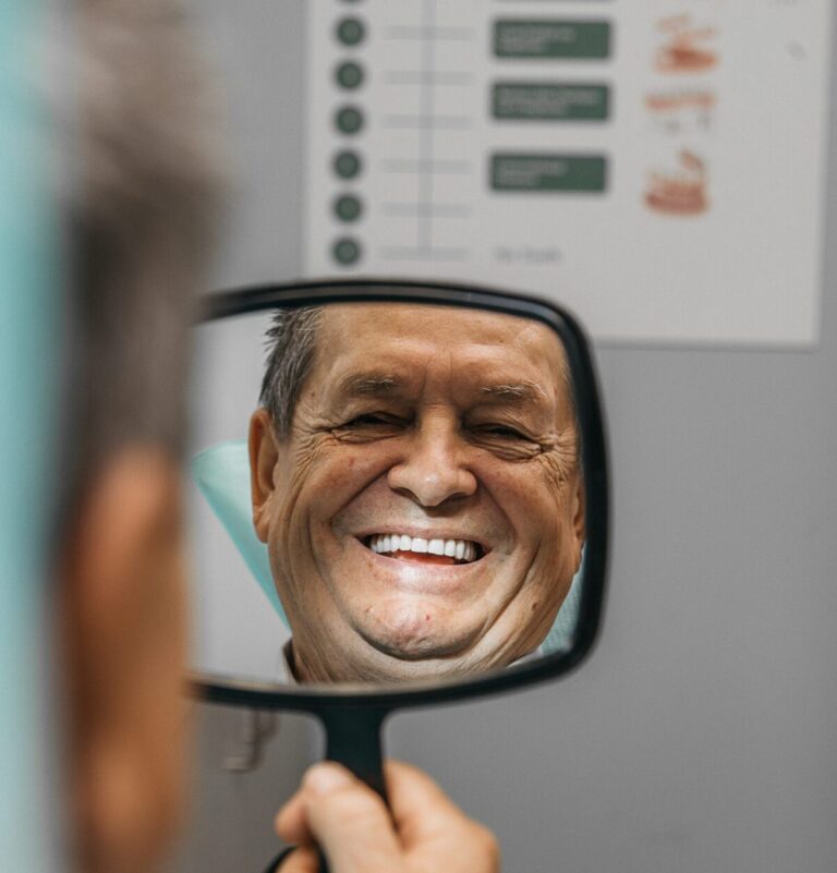 Patient Smiling with Dentures while looking at himself in a handheld mirror.