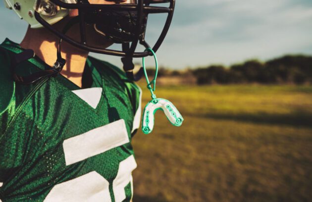 Football player on the field with a sports mouth guard attached to his helmet