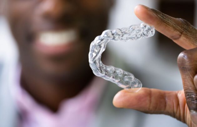 Smiling Man Holding A Clear Custom Mouth Guard From Halton Denture Clinic
