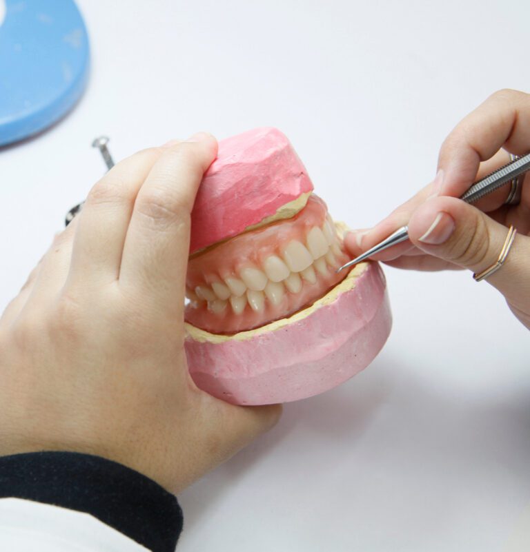 a denturist repairing a set of dentures with a metal tool